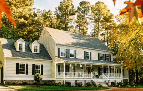 a wide view of a white suburban home with a front porch surrounded by trees